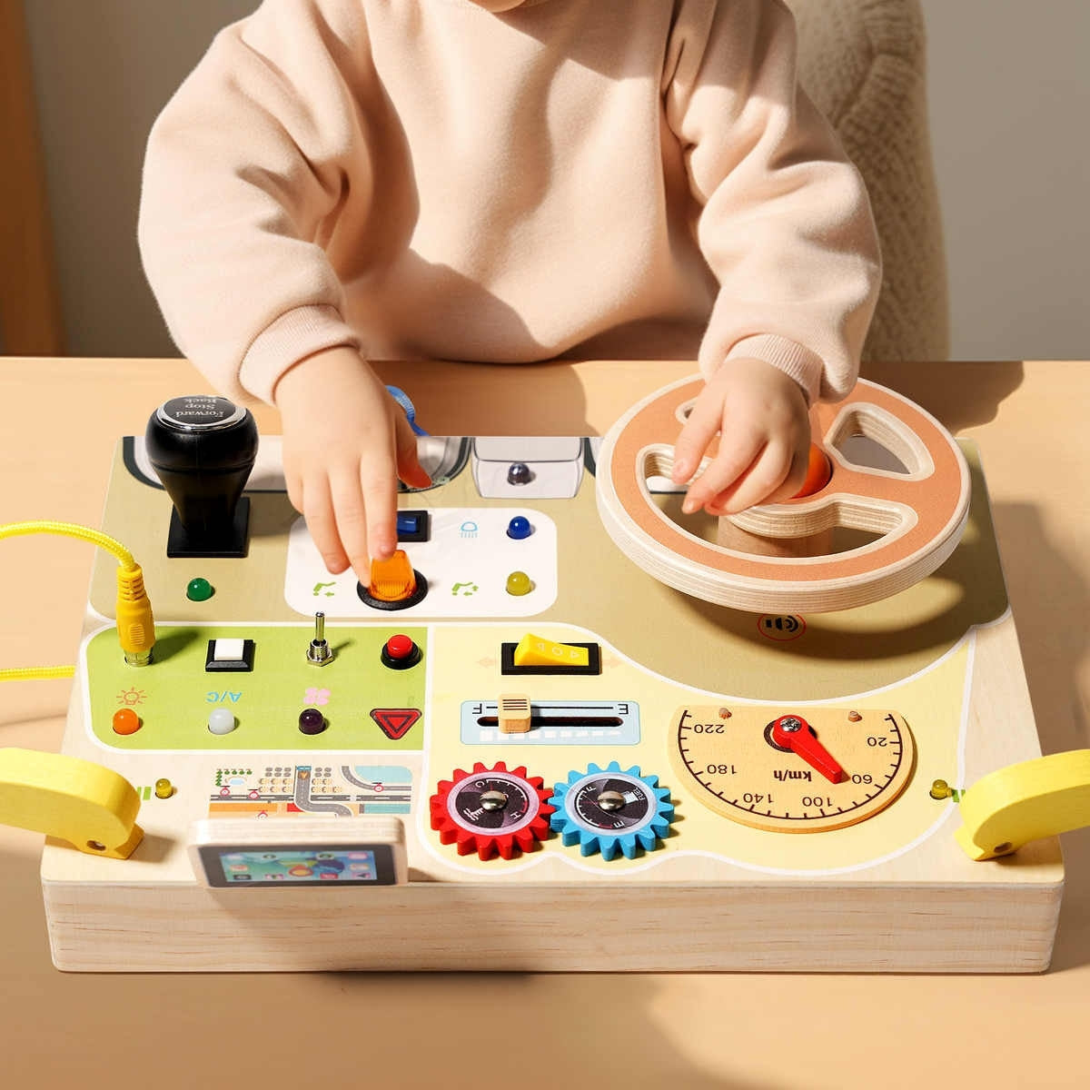 Toddler sitting at table playing with Montessori car dashboard steering wheel and switches
